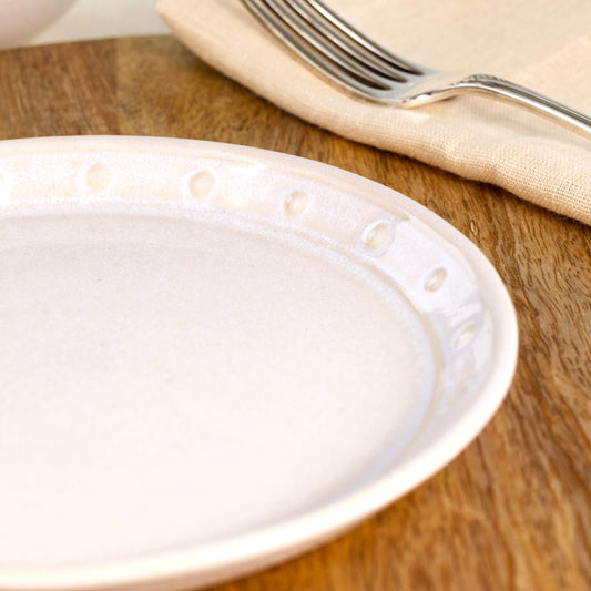 Close-up of a white stoneware small plate, highlighting the glossy speckled glaze, hand-finished dotted rim and simple minimalist ceramic finish