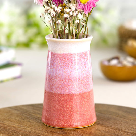Coral and white striped stoneware bud vase on a wooden surface, handcrafted double-dipped pottery in warm blush tones.