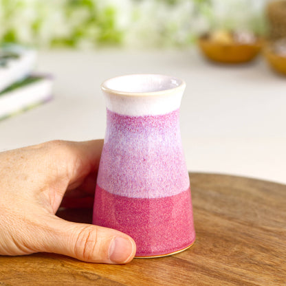 Cute handcrafted crimson and white mini bud vase held in hand, displaying a tapered form, speckled glaze texture, and softly banded two-tone design.