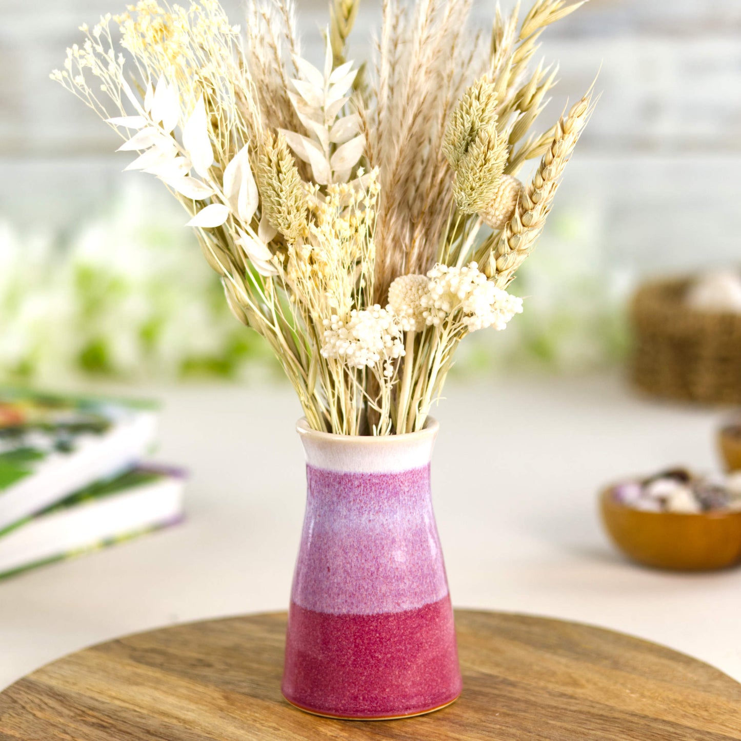 Wheel-thrown stoneware bud vase in deep crimson and soft blush-white tones, featuring a banded two-tone finish and tapered silhouette, styled with natural dried grasses for rustic décor.