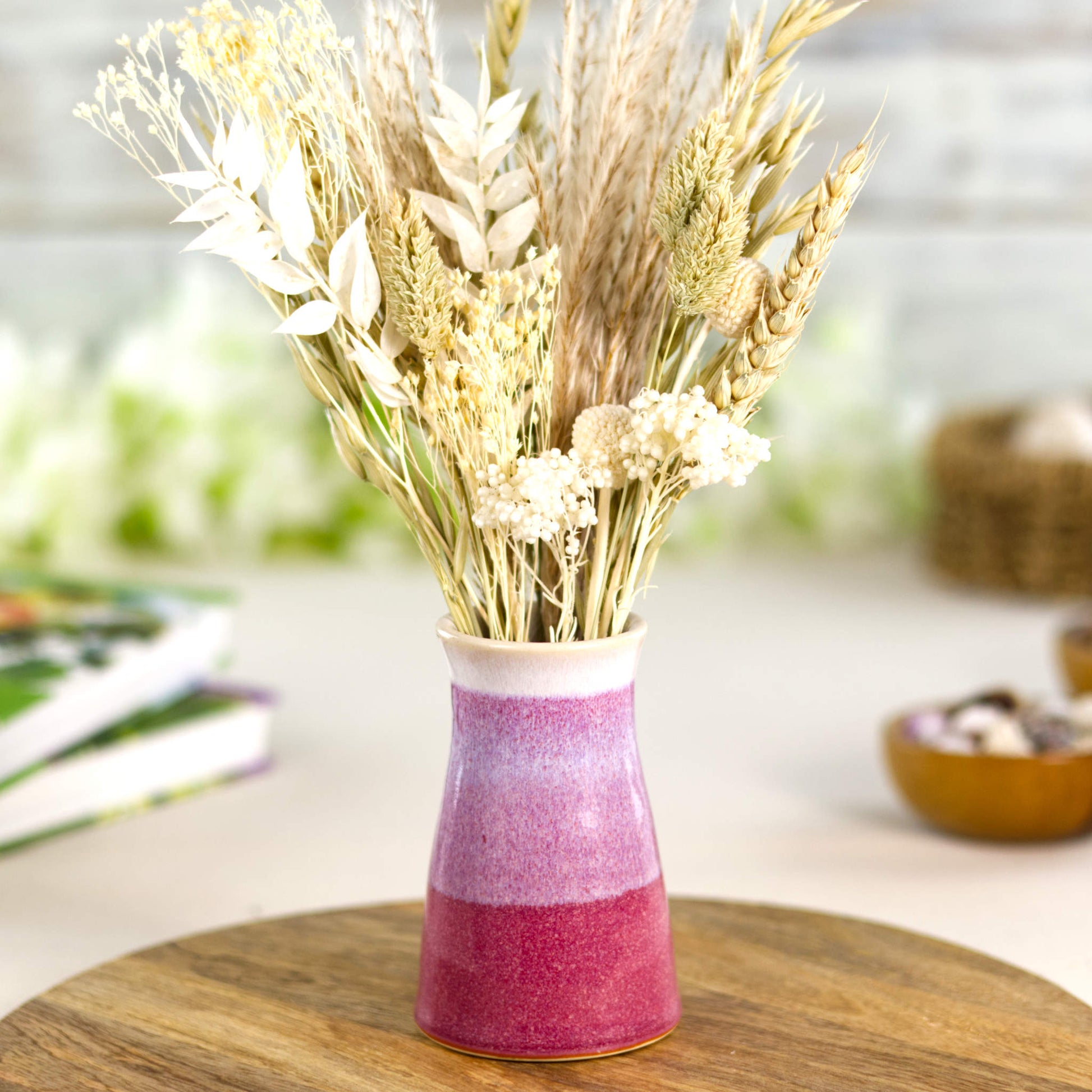 Wheel-thrown stoneware bud vase in deep crimson and soft blush-white tones, featuring a banded two-tone finish and tapered silhouette, styled with natural dried grasses for rustic décor.