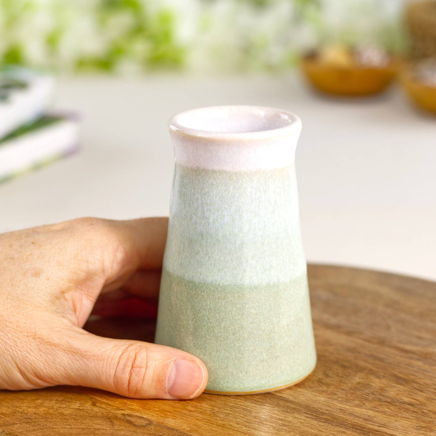 Hand-thrown Pale Green and white conical bud vase held in hand, a small artisan stoneware vase ideal for single stems and shelf styling.