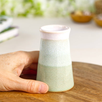 Hand-thrown Pale Green and white conical bud vase held in hand, a small artisan stoneware vase ideal for single stems and shelf styling.