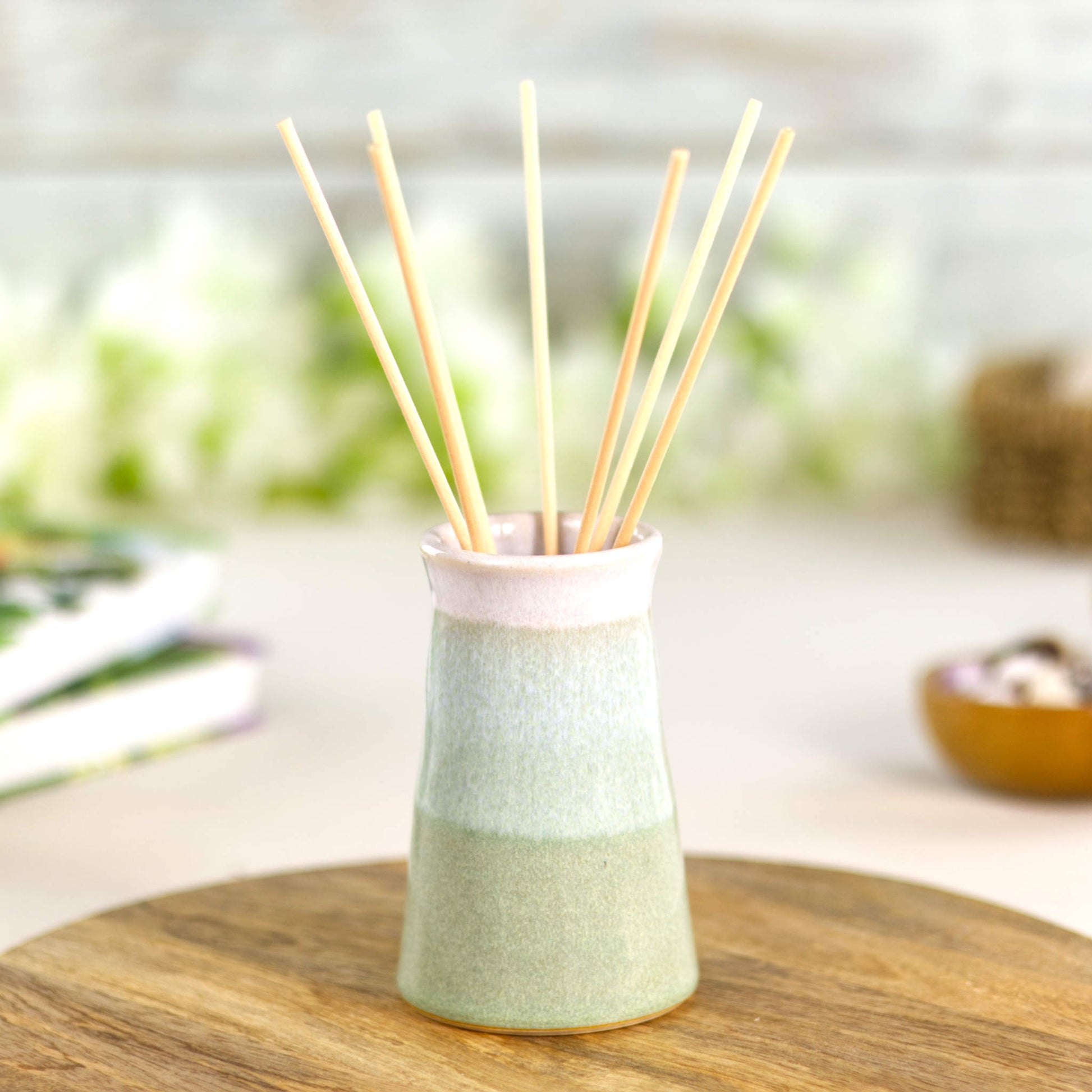 Pastel Green and white ceramic bud vase used as a reed diffuser, a handcrafted conical stoneware vessel for spa-inspired home fragrance.