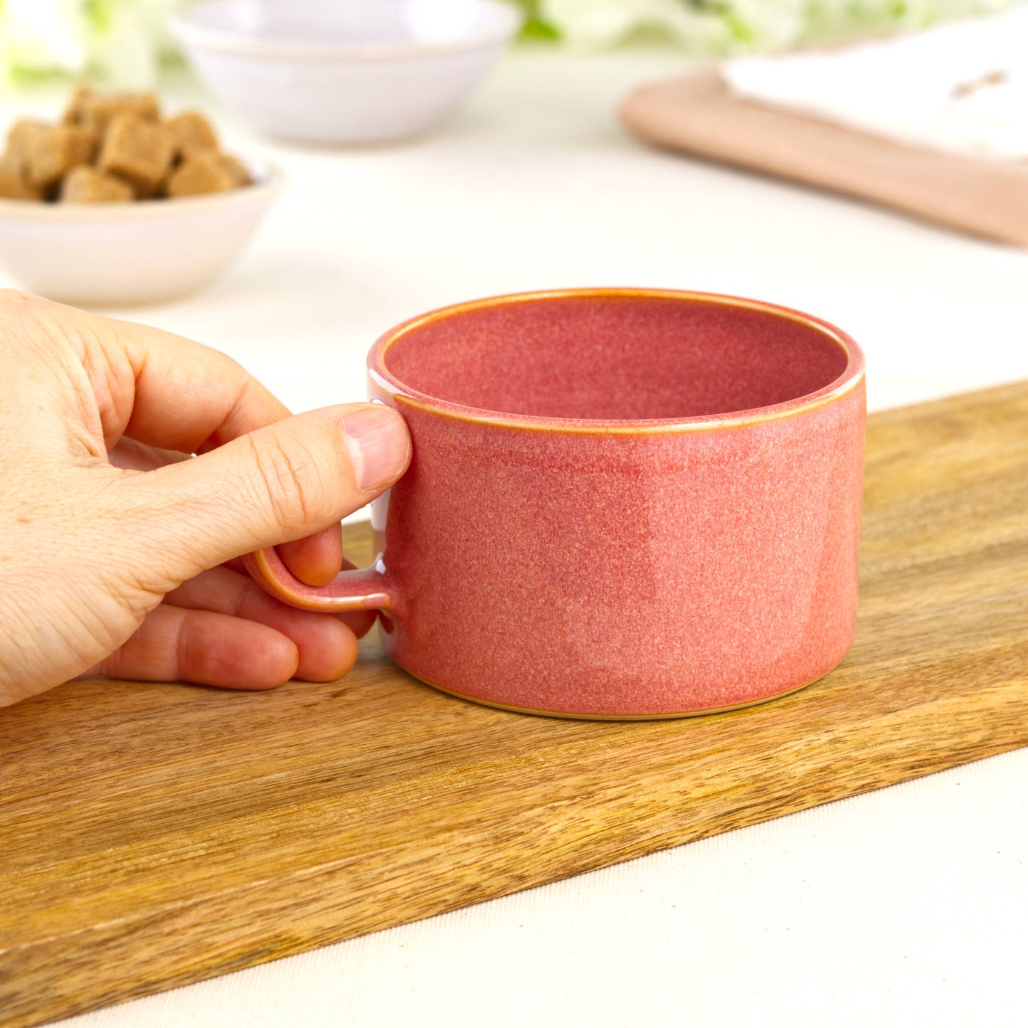 Coral ceramic coffee cup held in hand, wheel-thrown café mug with broad rim for cappuccino foam and barista style pours