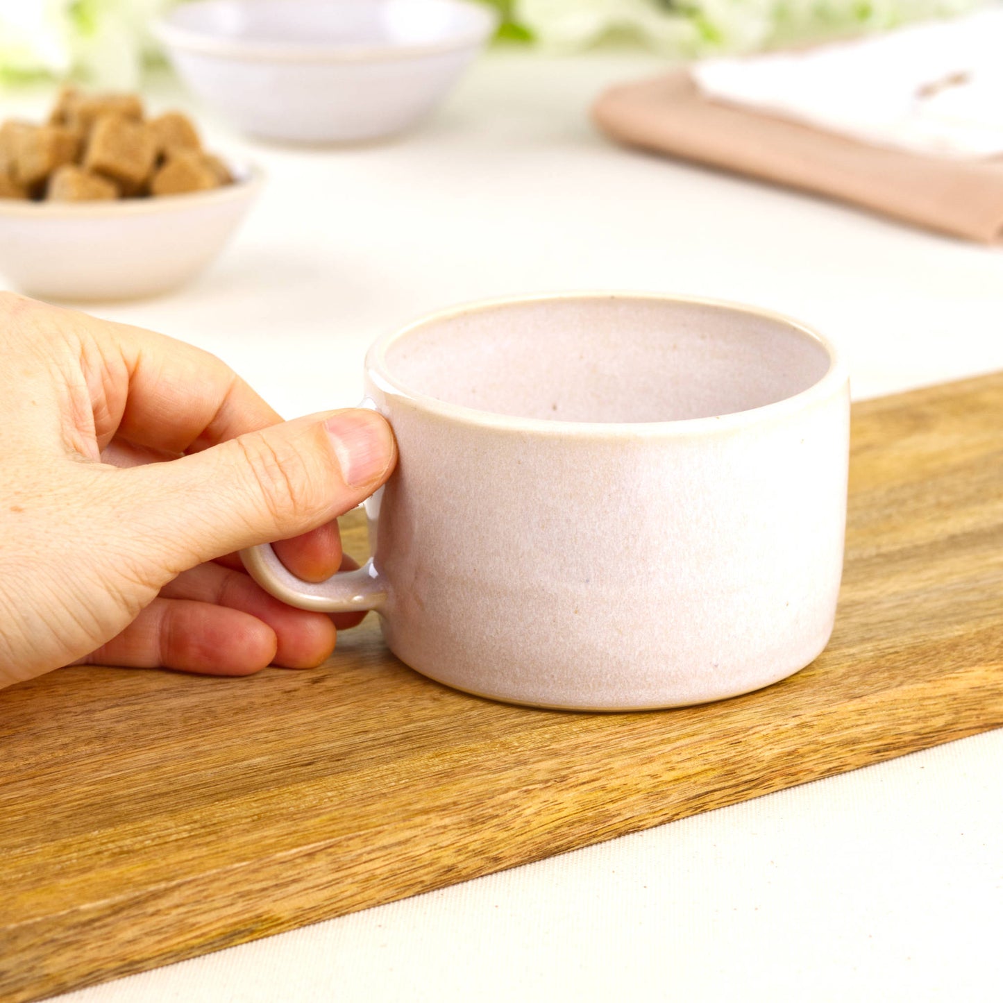 White ceramic coffee cup held in hand, wheel-thrown café mug with wide rim for cappuccino foam and silky microfoam pours