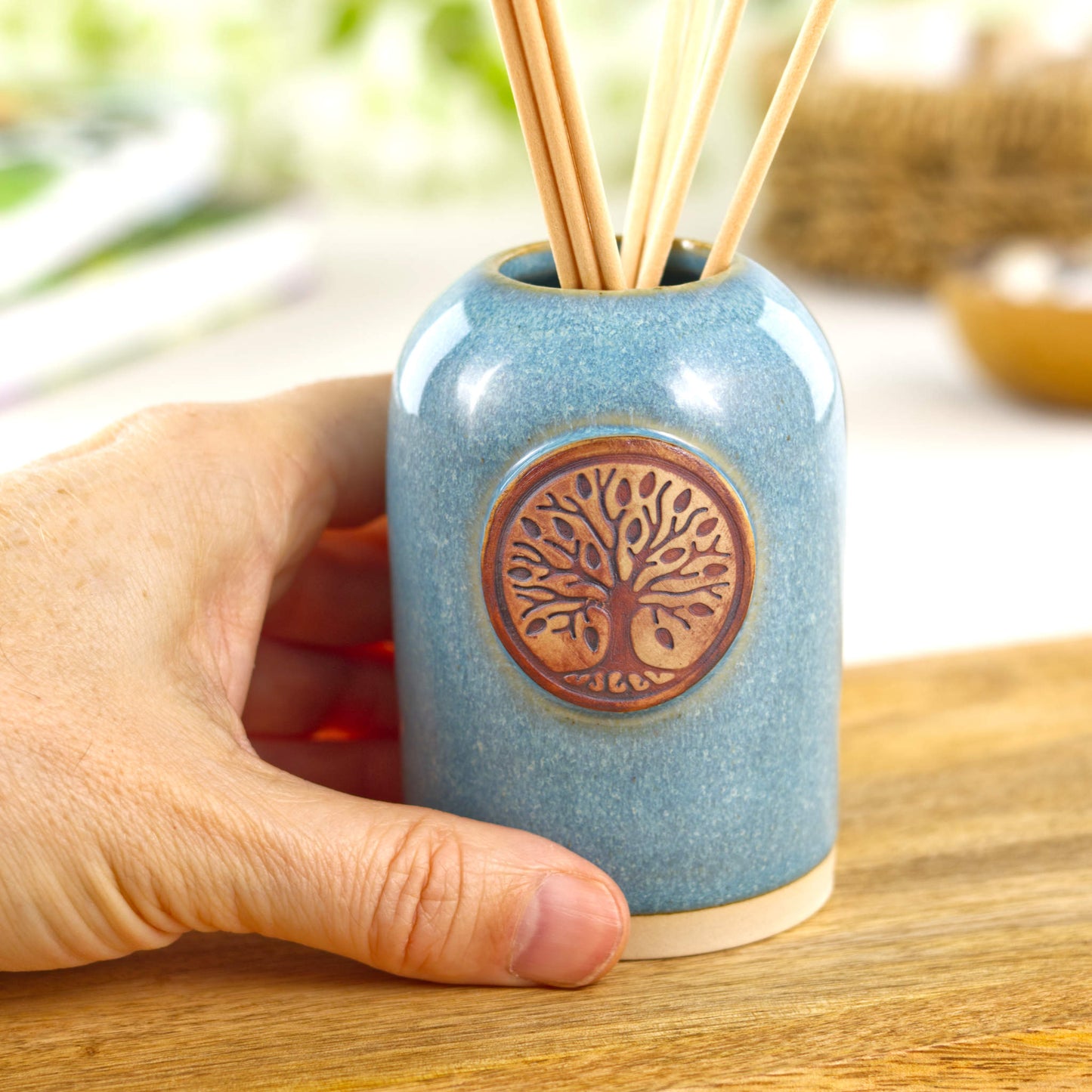 Small handmade coastal blue reed diffuser shown in hand for size with ceramic world tree front detail