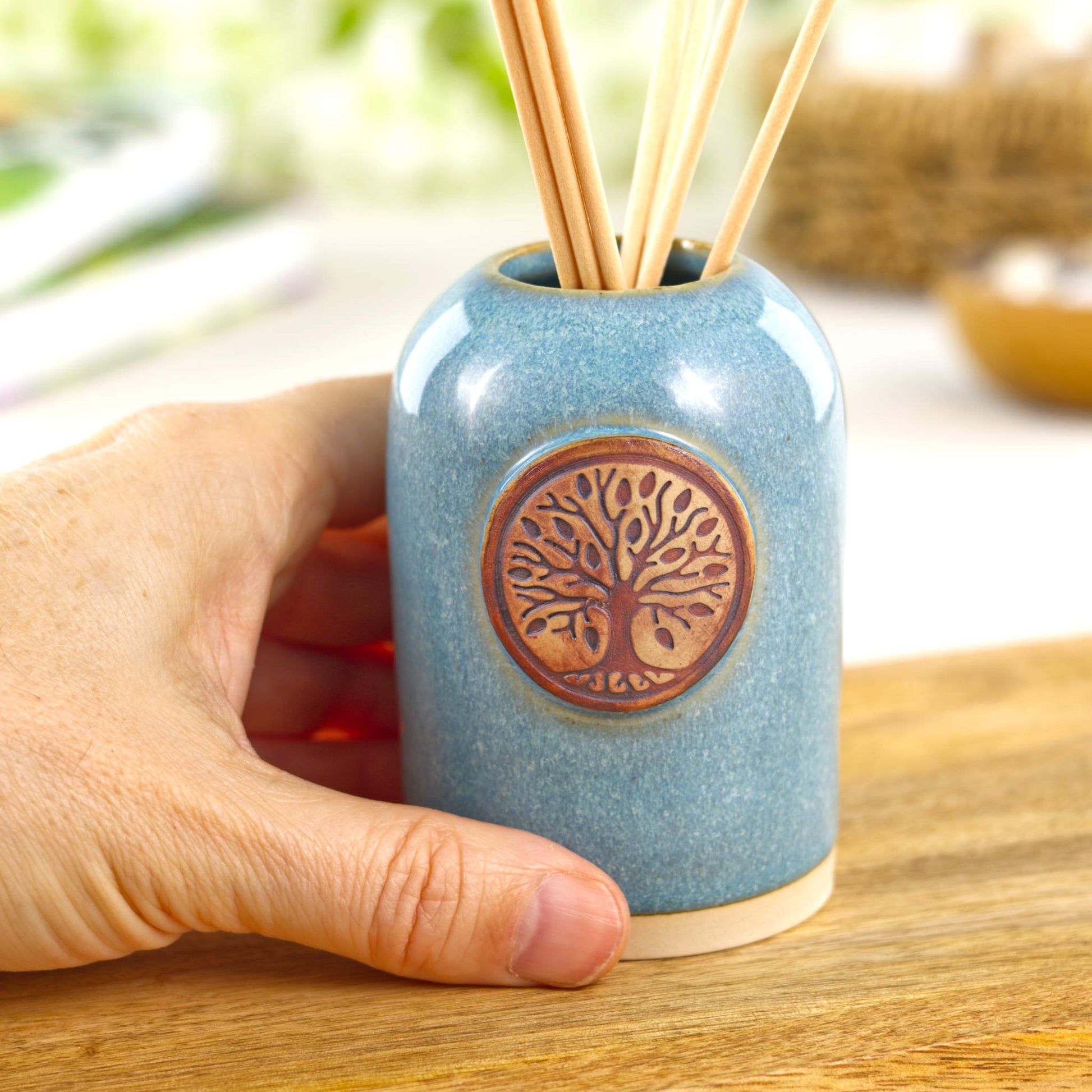 Small handmade coastal blue reed diffuser shown in hand for size with ceramic world tree front detail