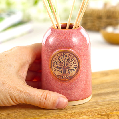 Small handmade coral refillable fragrance diffuser shown in hand for size with decorative botanical badge