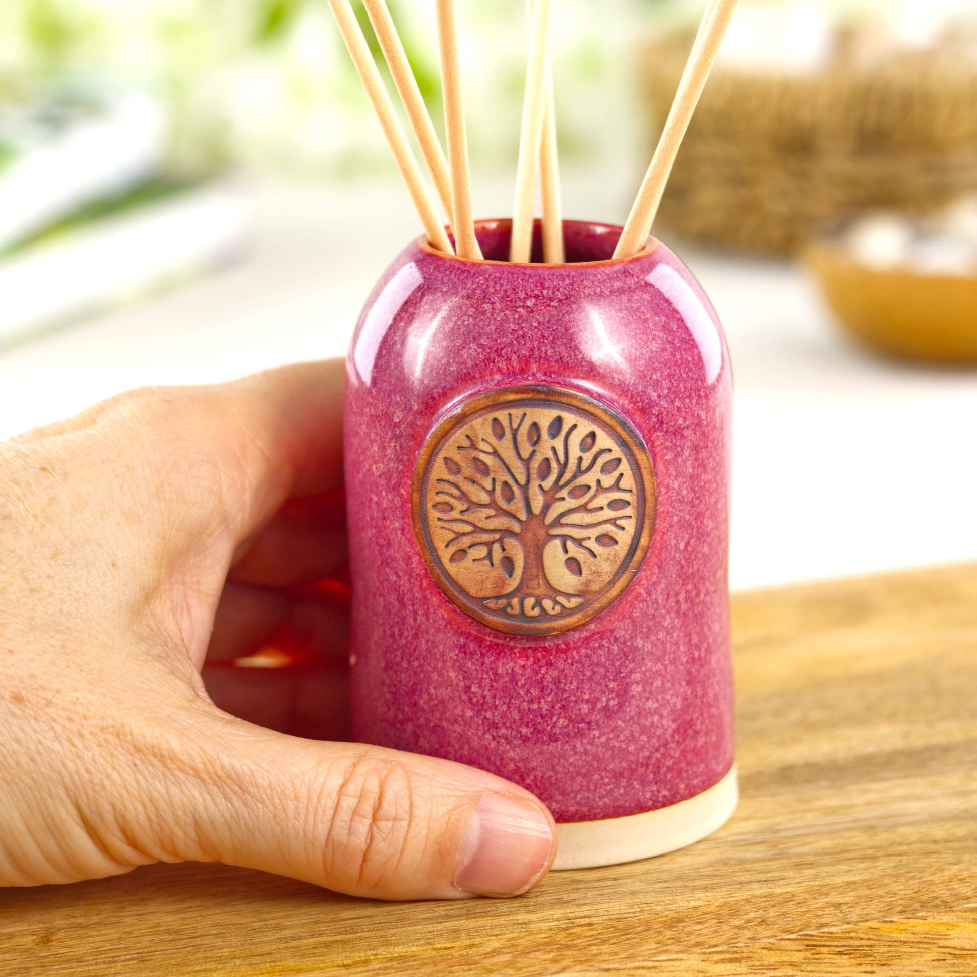 Small handmade crimson refillable scent diffuser shown in hand for size with woodland emblem detail