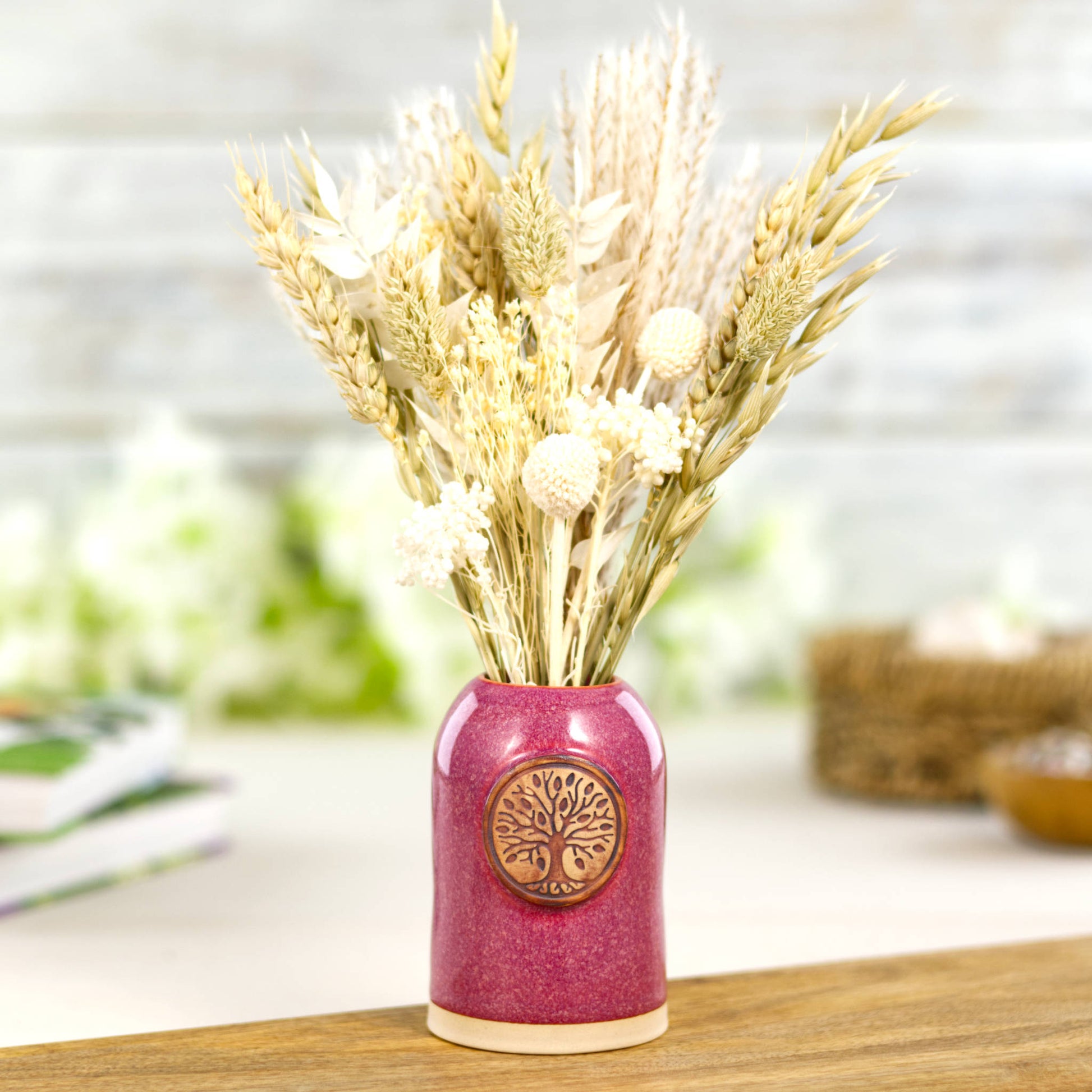 Crimson ceramic bud vase with dried flowers in rustic botanical arrangement and nature inspired medallion