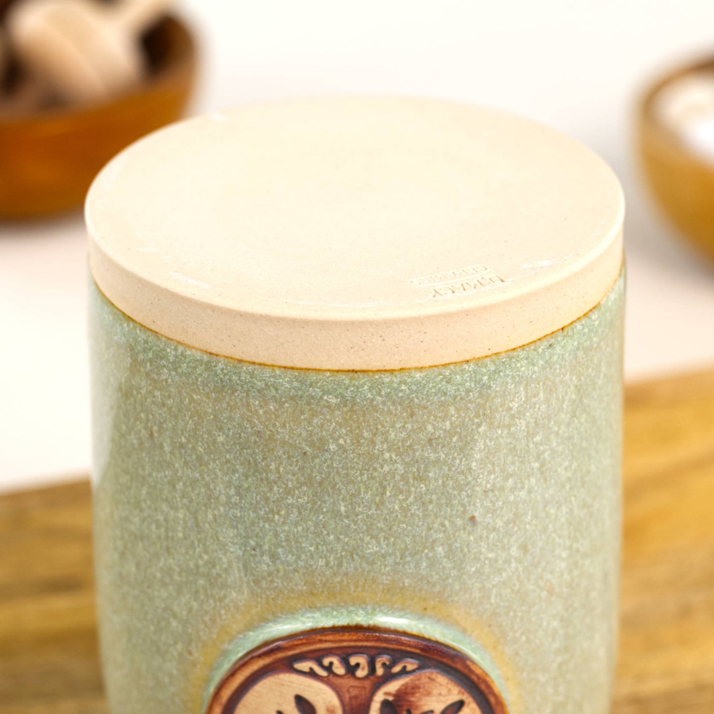 Base of handmade pale green ceramic diffuser vessel showing smooth unglazed stoneware foot and maker mark