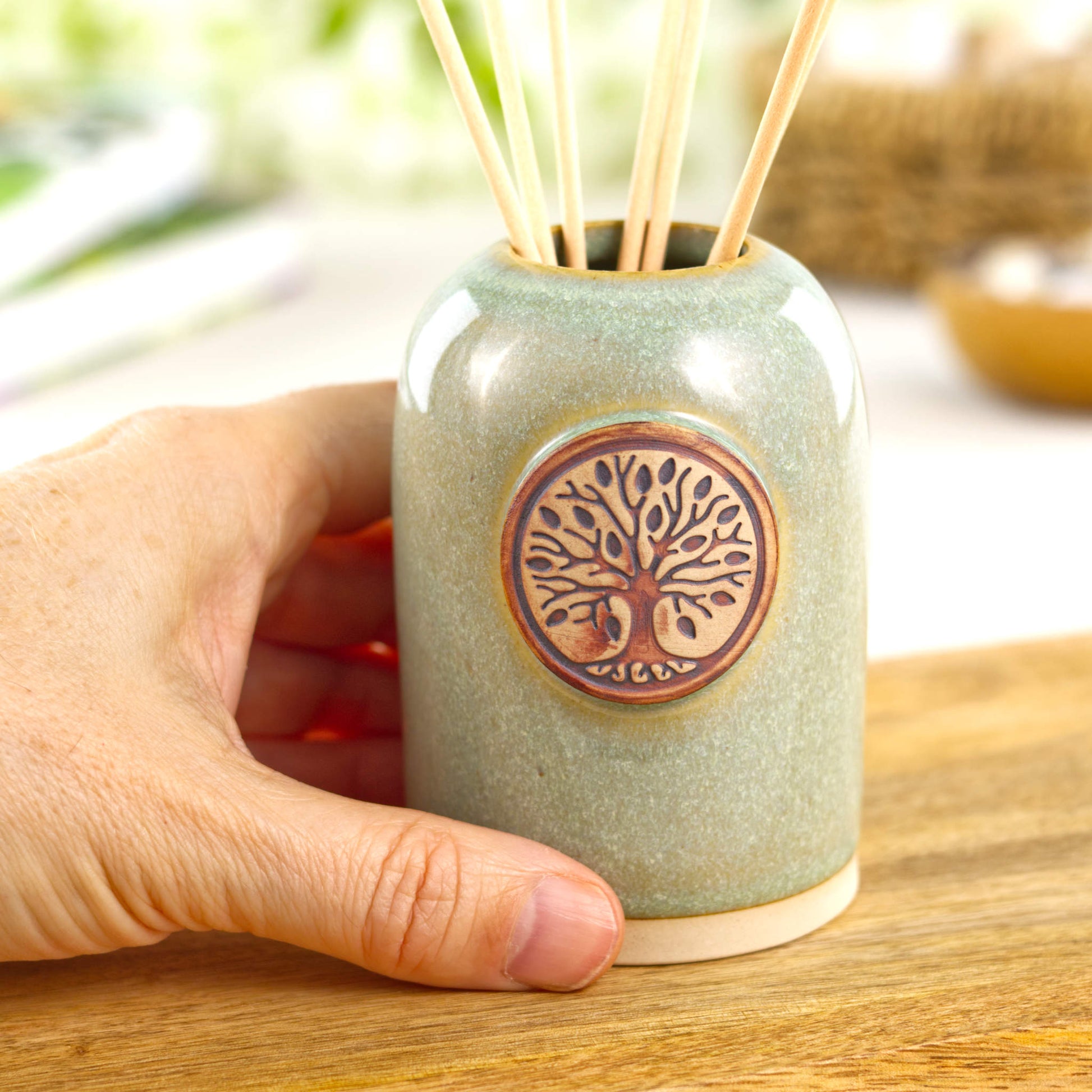 Small handmade pale green refillable fragrance diffuser shown in hand for size with botanical badge detail