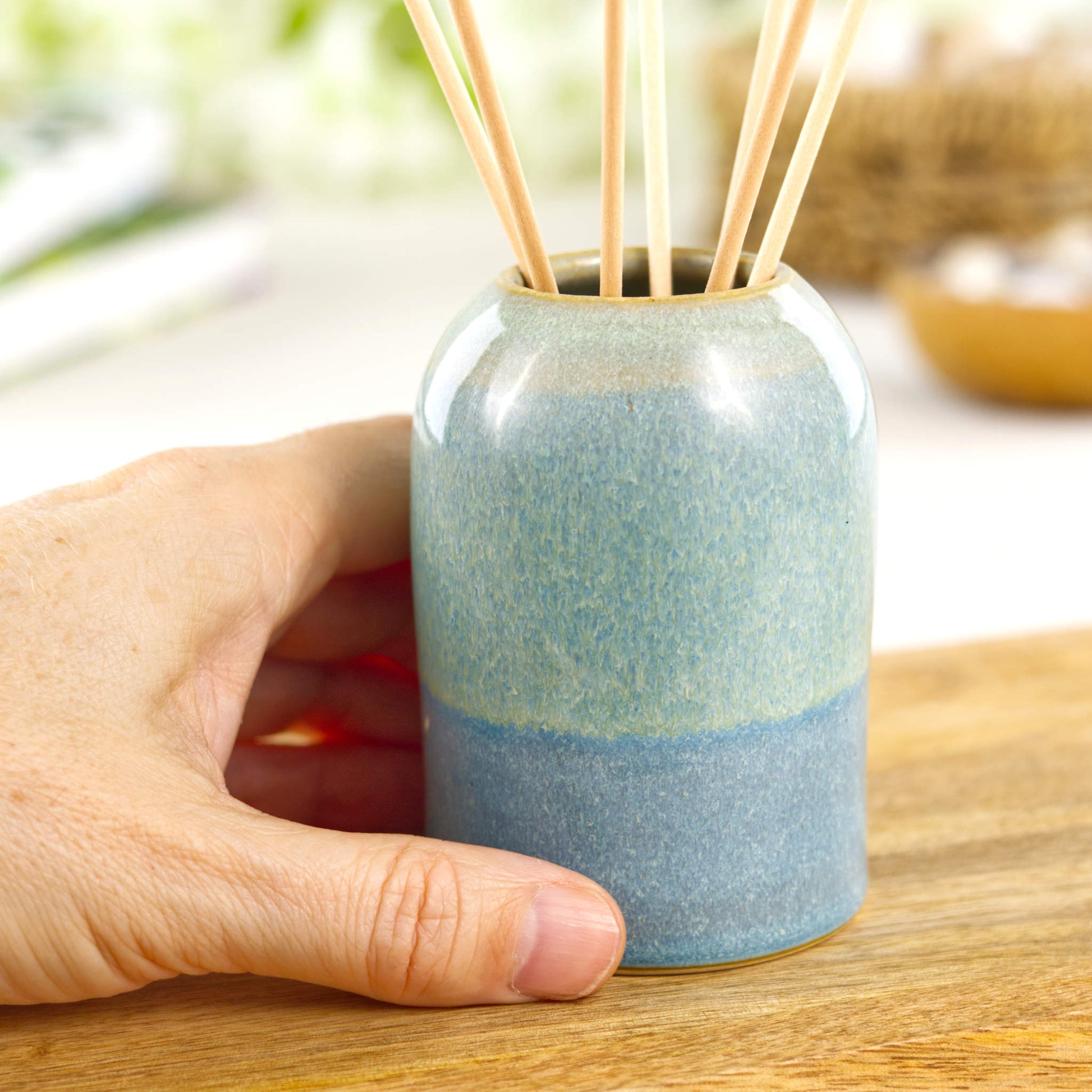Small handmade ceramic reed diffuser in Coastal Blue and Pale Green shown in hand for size reference, compact pottery diffuser for shelf styling
