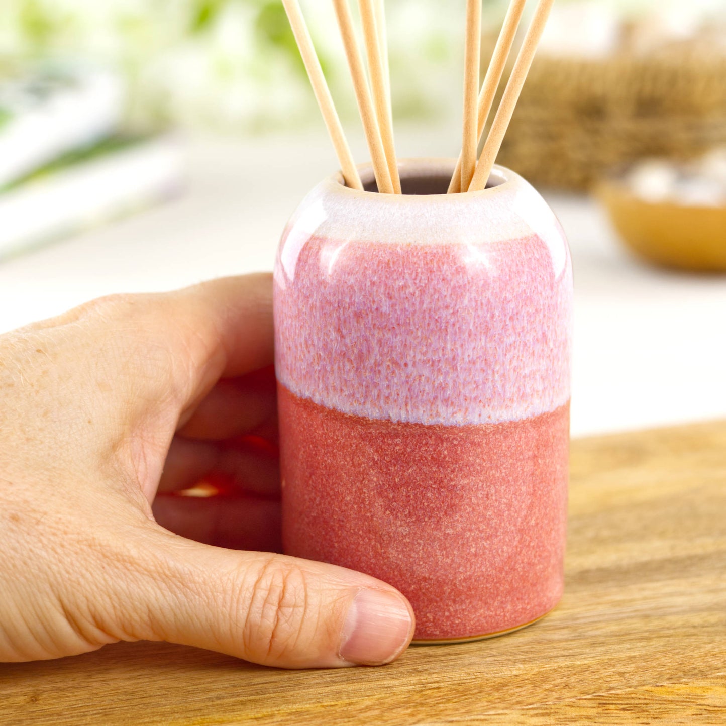 Small Coral and White handmade home fragrance pot shown in hand for size, compact shelf decor piece