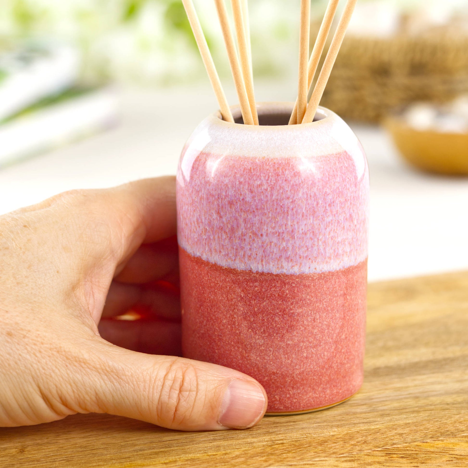 Small Coral and White handmade home fragrance pot shown in hand for size, compact shelf decor piece