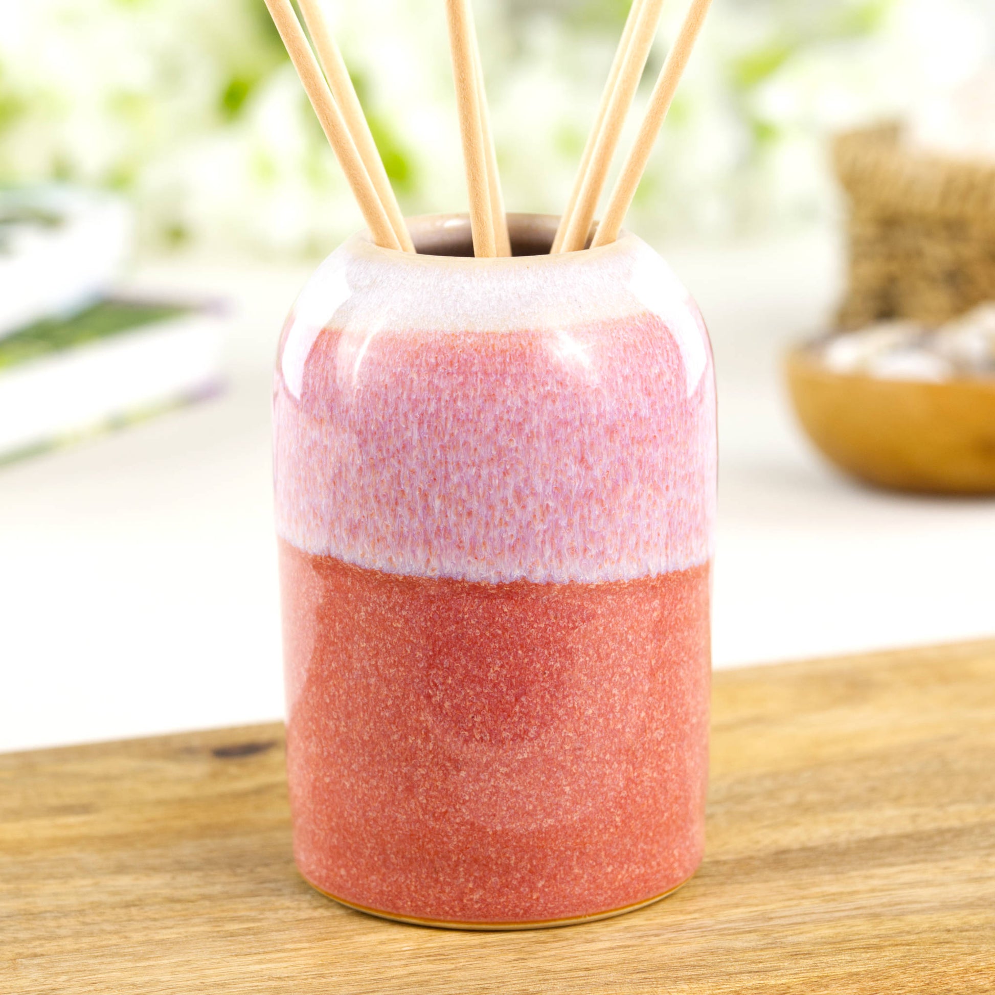Warm Coral and White stoneware reed diffuser with modern rounded form on wooden surface
