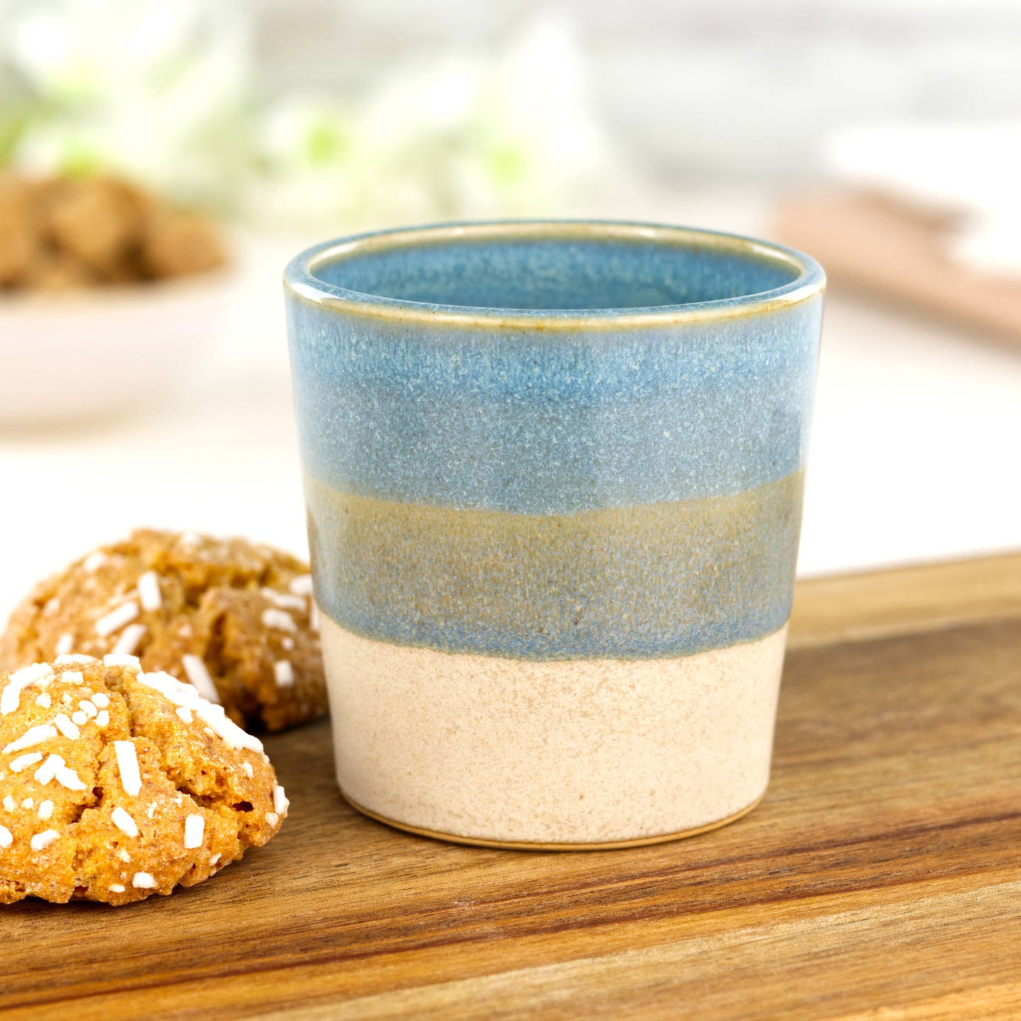 Two-tone ceramic espresso cup in Coastal Blue and sandy oat glaze on wooden board with amaretti biscuits