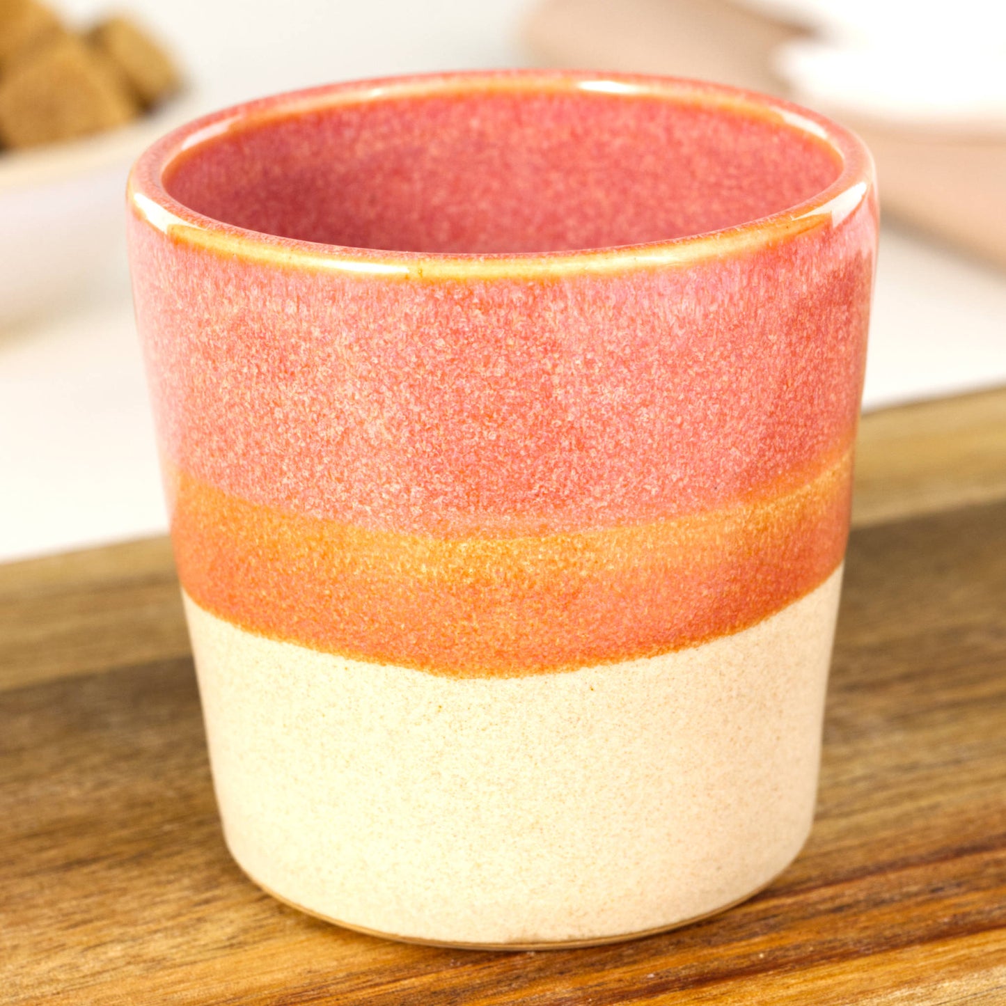 Handmade banded espresso cup close-up showing warm coral glaze and satin matte sandy base