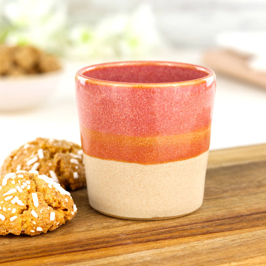 Two-tone ceramic espresso cup in Coral and sandy oat glaze on wooden board with biscuits