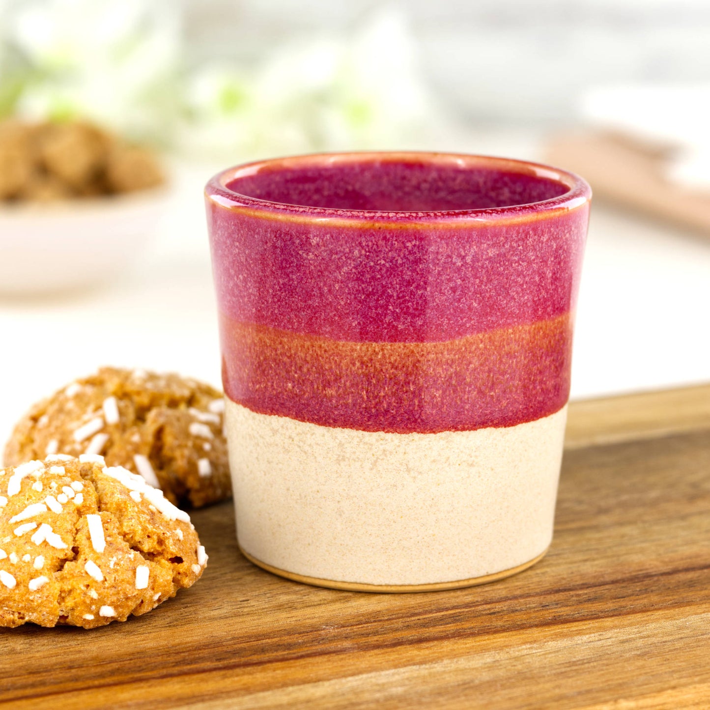Two-tone ceramic espresso cup in Crimson and sandy oat glaze on wooden board with biscuits