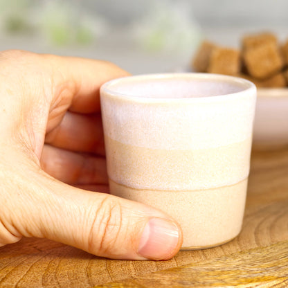 White and cream coloured espresso cup being held in the hand for scale