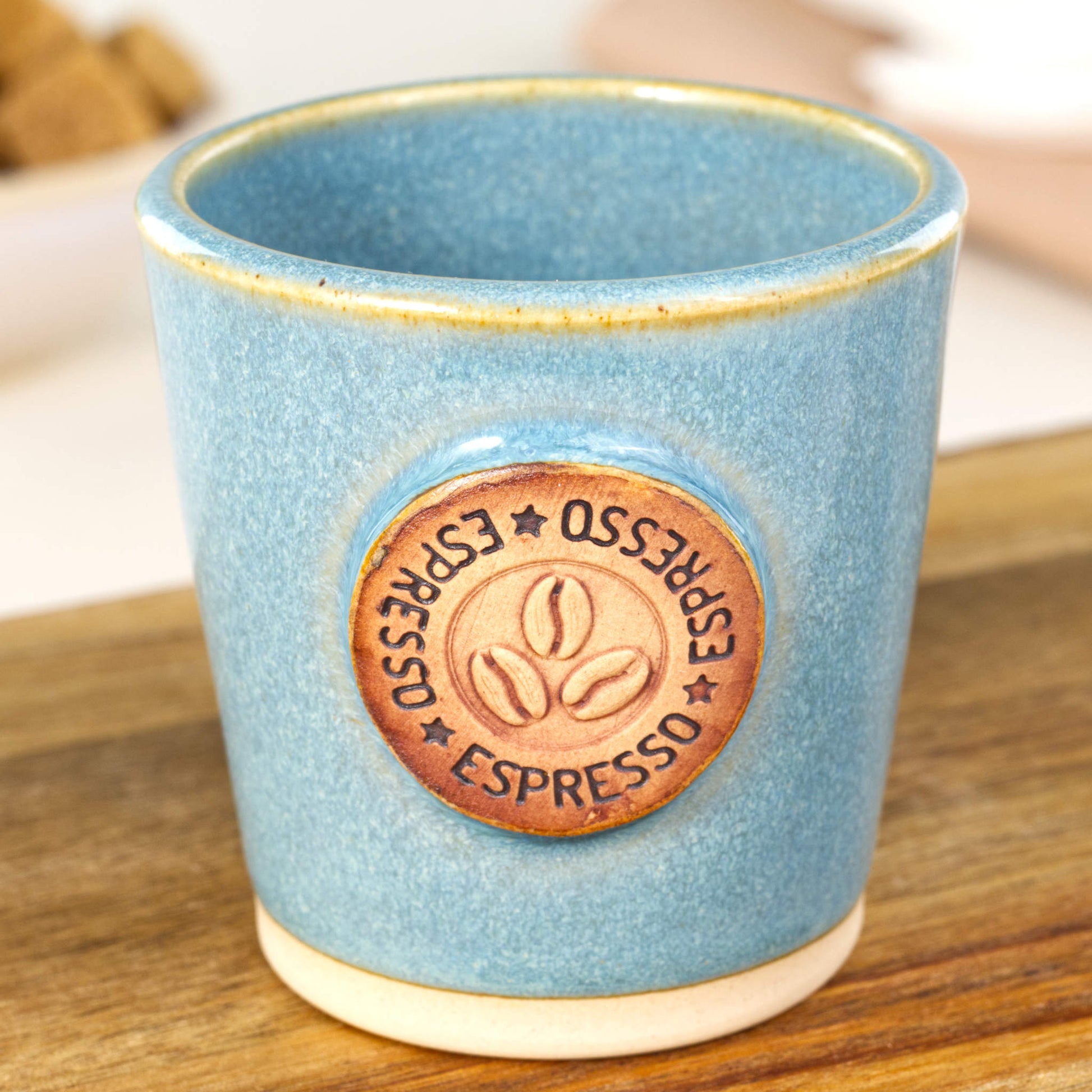 Handmade espresso cup close-up showing coffee bean badge and glossy speckled glaze