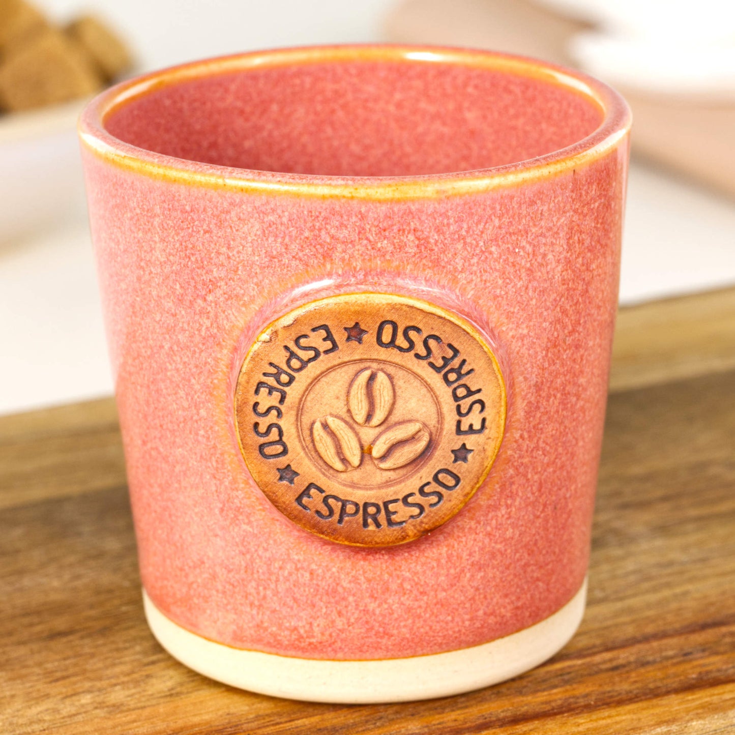 Handmade espresso cup close-up showing coffee bean badge and warm coral glaze texture