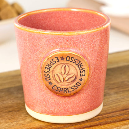 Handmade espresso cup close-up showing coffee bean badge and warm coral glaze texture