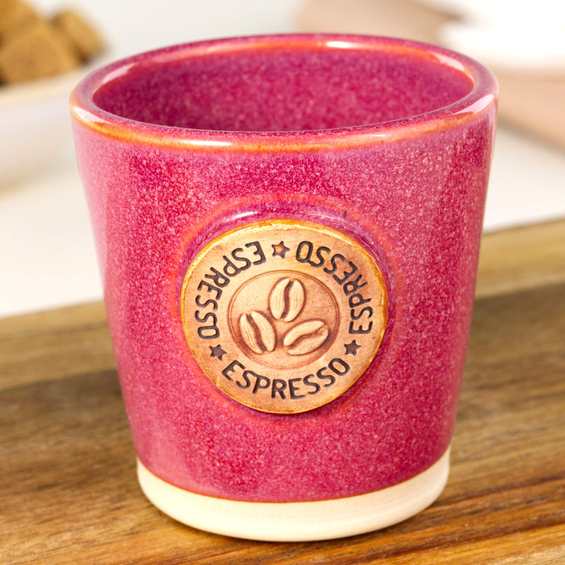Handmade espresso cup close-up showing coffee bean badge and rich crimson glaze finish