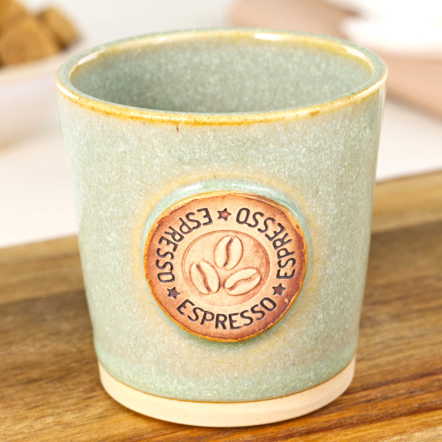 Handmade espresso cup close-up showing coffee bean badge and glossy pale green glaze detail