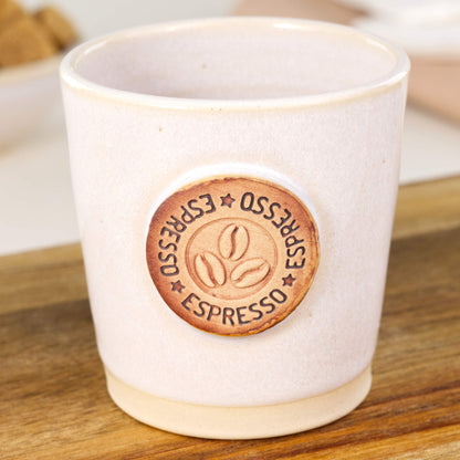 Handmade espresso cup close-up showing coffee bean badge and clean white glaze finish