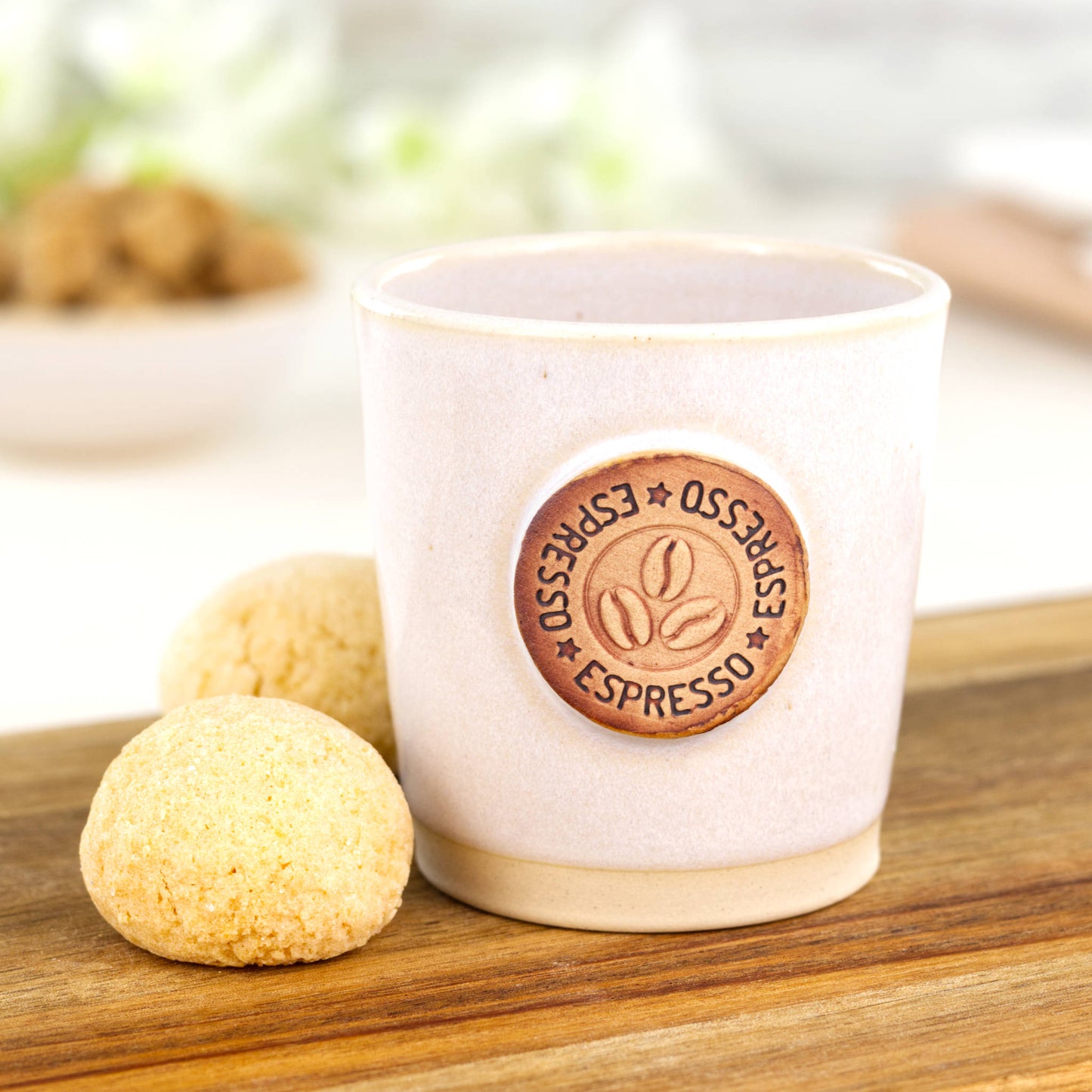 White ceramic espresso cup with coffee bean motif styled with biscuits on wooden board