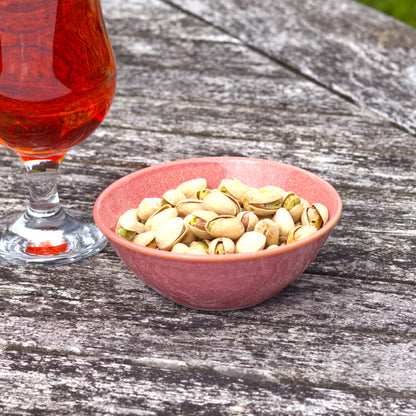 Coral stoneware nibbles bowl with pistachios beside a drink, handmade in a small UK pottery studio for sharing with friends