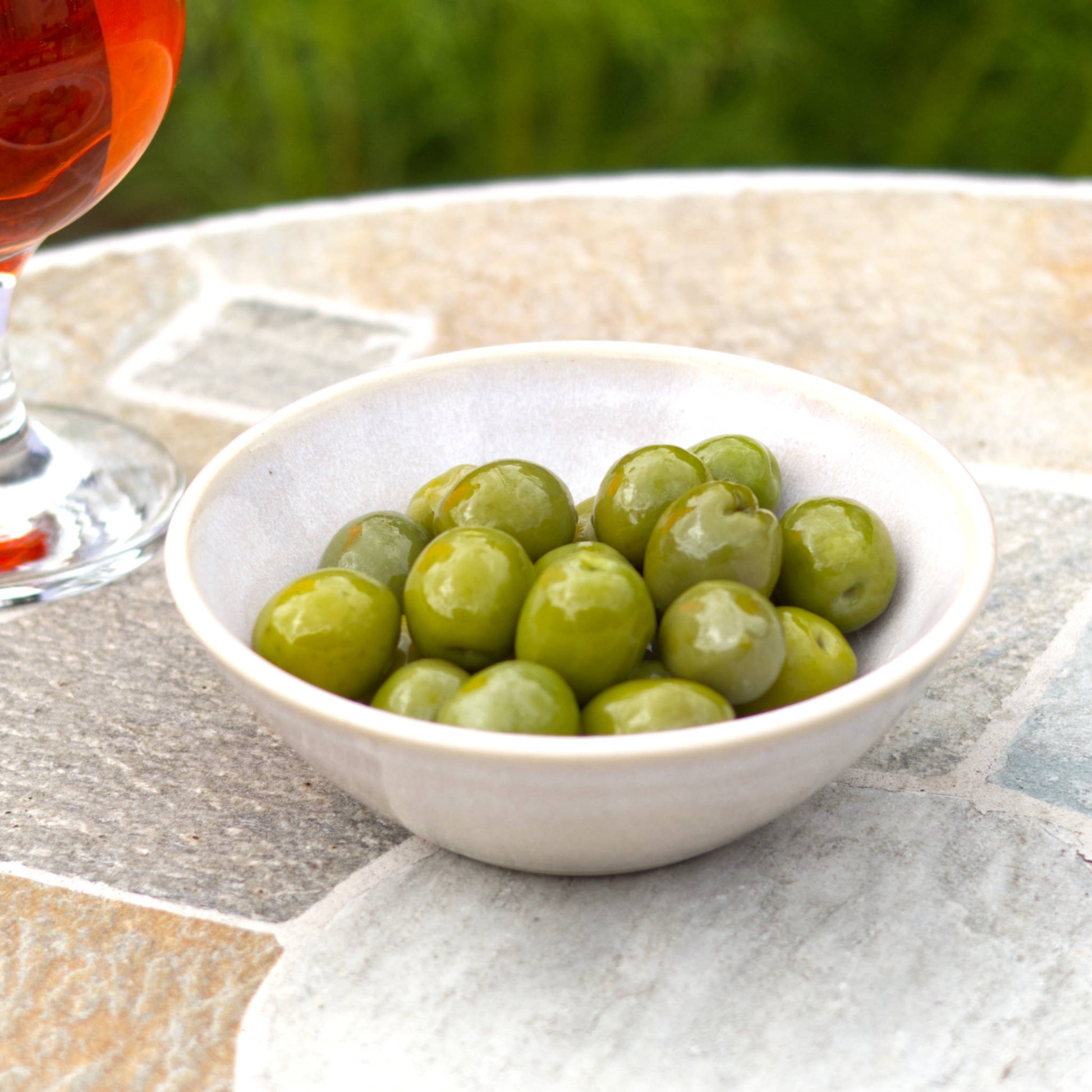 White handmade ceramic olive bowl filled for garden drinks, a small stoneware snack bowl with clean rustic table styling