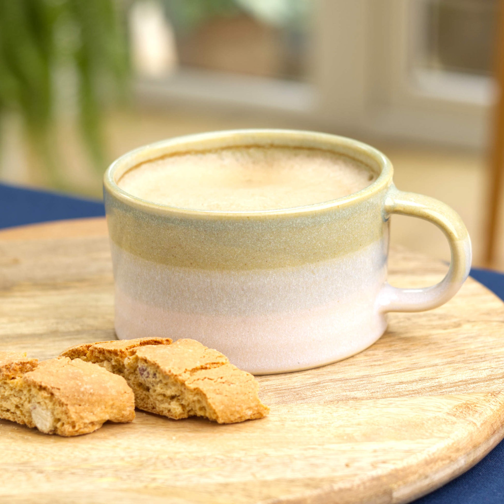 Pale Green and White stoneware cappuccino cup filled with fresh coffee on serving board with biscotti, cosy kitchen coffee moment