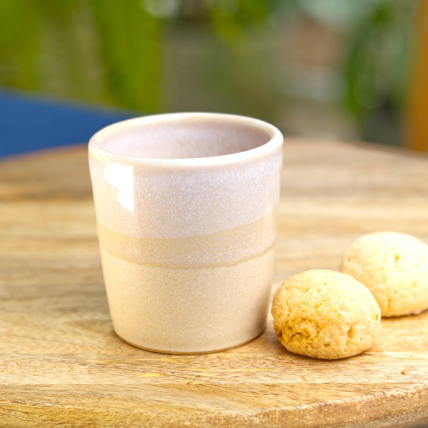 A glossy white and satin beige espresso cup, made an a small pottery studio, sits alongside sone mini biscuits