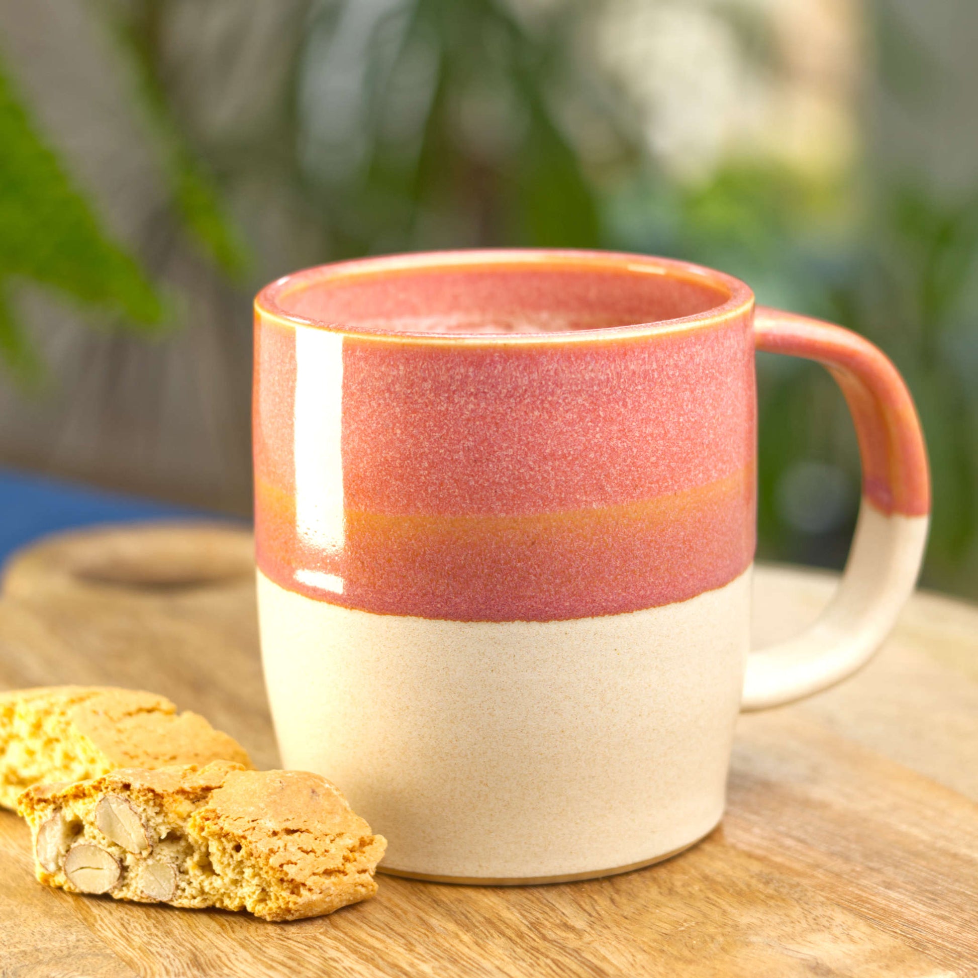 Coral and Sand handmade hot chocolate mug filled with frothy coffee on a wooden board with biscotti, wheel-thrown stoneware made in my Sussex pottery studio