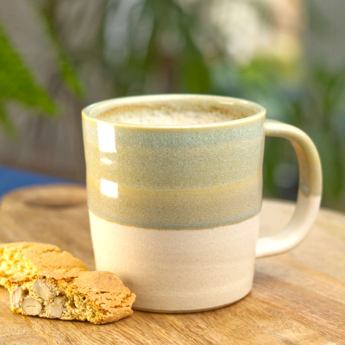 Pale Green and Sand handmade hot chocolate mug filled with frothy coffee on a wooden board with biscotti, wheel-thrown stoneware from my Sussex pottery studio
