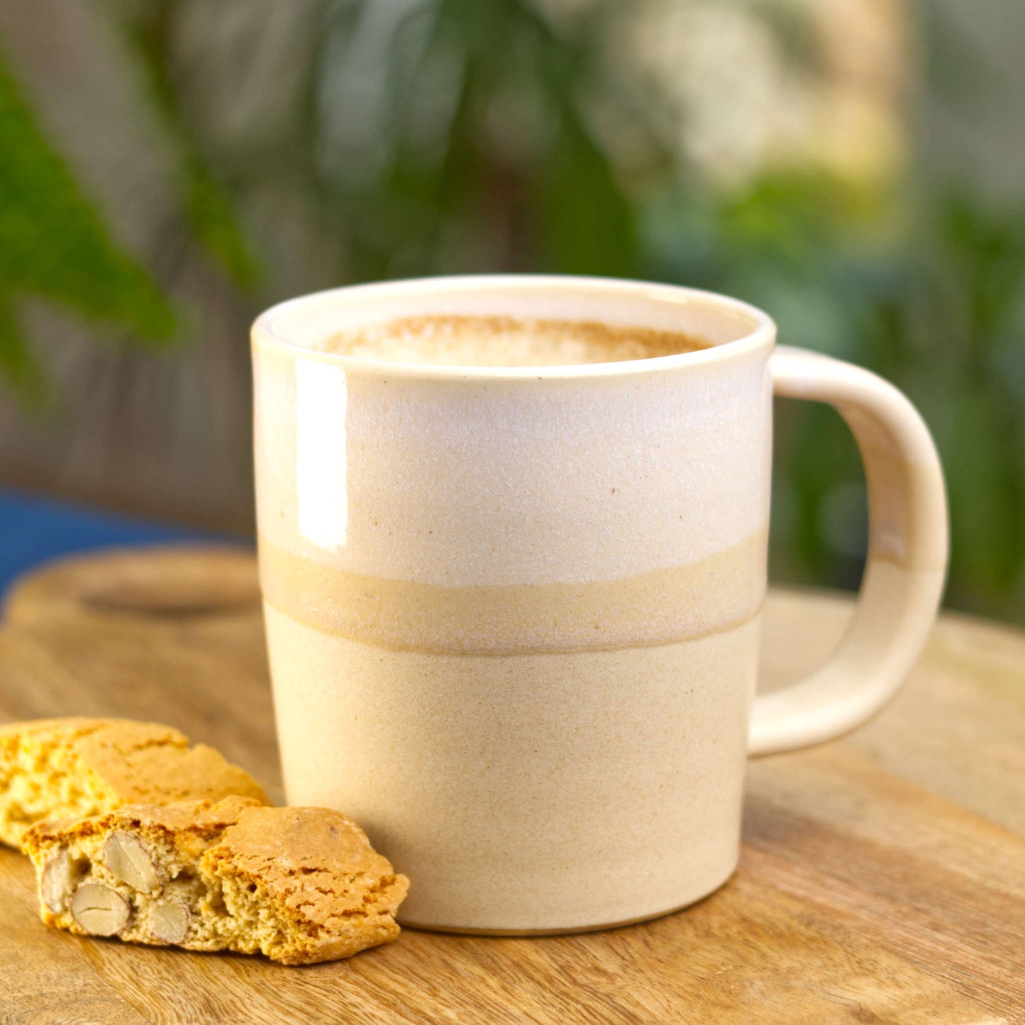 White and Sand handmade ceramic mug filled with frothy coffee on a wooden board with biscotti, a scandi style stoneware mug made in my Sussex studio