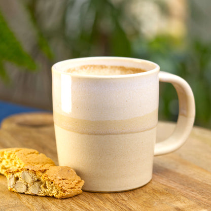 White and Sand handmade ceramic mug filled with frothy coffee on a wooden board with biscotti, a scandi style stoneware mug made in my Sussex studio