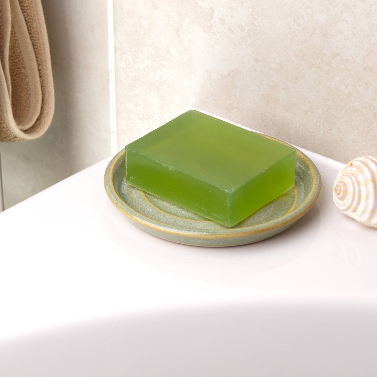 Pale green ceramic soap dish holding natural green soap bar beside bath