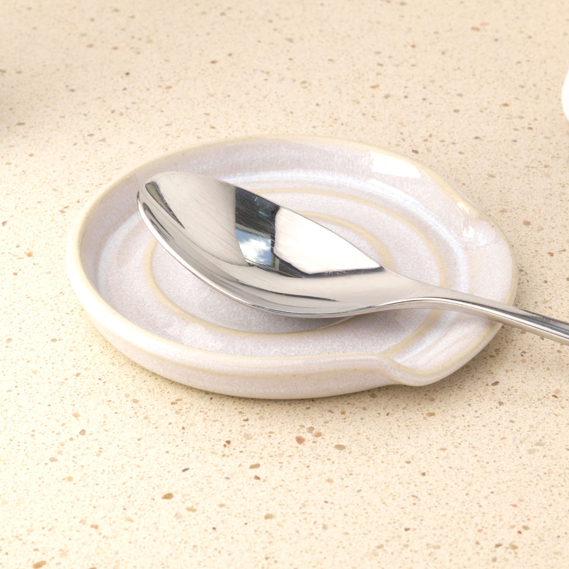 White ceramic spoon rest holding tablespoon, practical handmade utensil stand for tidy countertops and minimalist cooking spaces