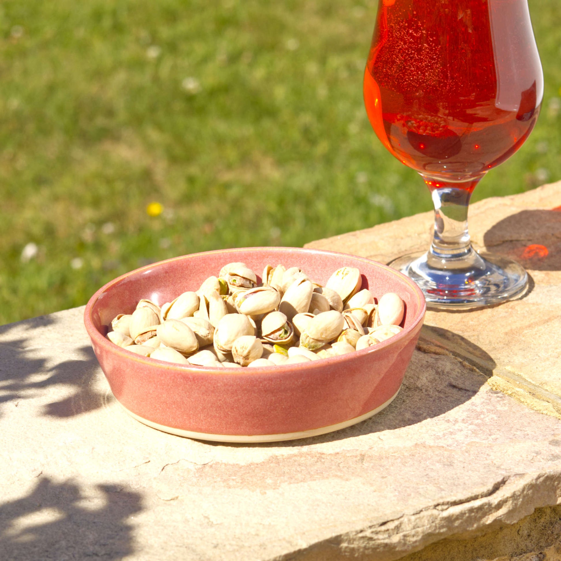 Coral handmade tapas bowl filled with pistachios, styled outdoors for aperitif snacks, party nibbles, garden entertaining and relaxed summer sharing