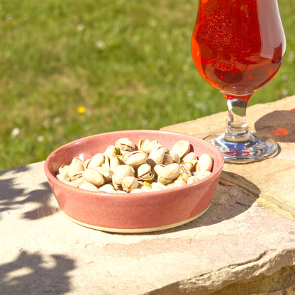 Coral handmade tapas bowl filled with pistachios, styled outdoors for aperitif snacks, party nibbles, garden entertaining and relaxed summer sharing