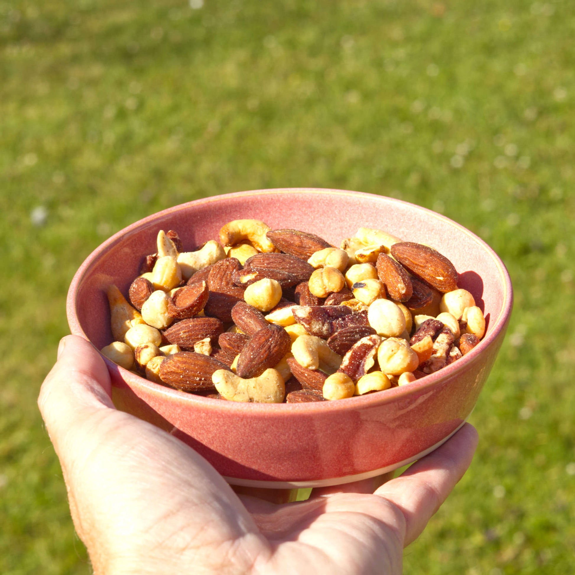 Handmade Coral ceramic tapas bowl held in the hand and filled with mixed nuts, a shallow stoneware dish for grazing boards, bar snacks and casual outdoor dining