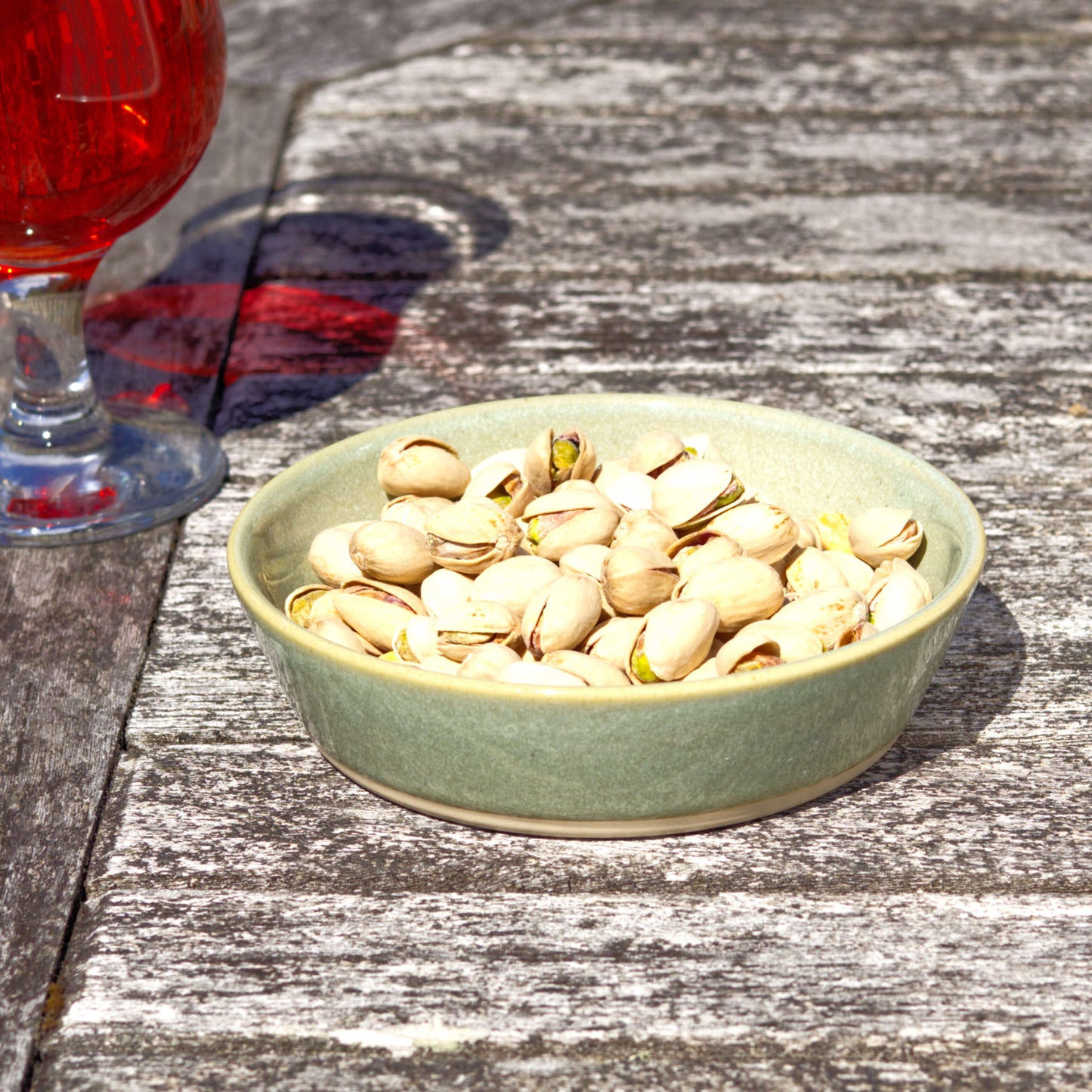 Pale Green stoneware tapas bowl filled with pistachios on a rustic outdoor table, ideal for bar snacks, antipasti, olives and casual sharing food