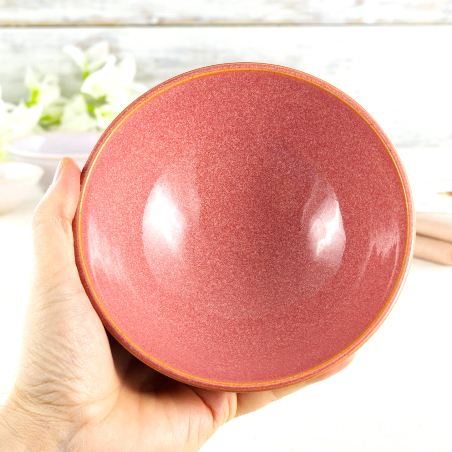 Medium handmade bowl held in the hand, glazed in Coral with a soft uplifting colour, perfect for soups, grain bowls or everyday artisan tableware