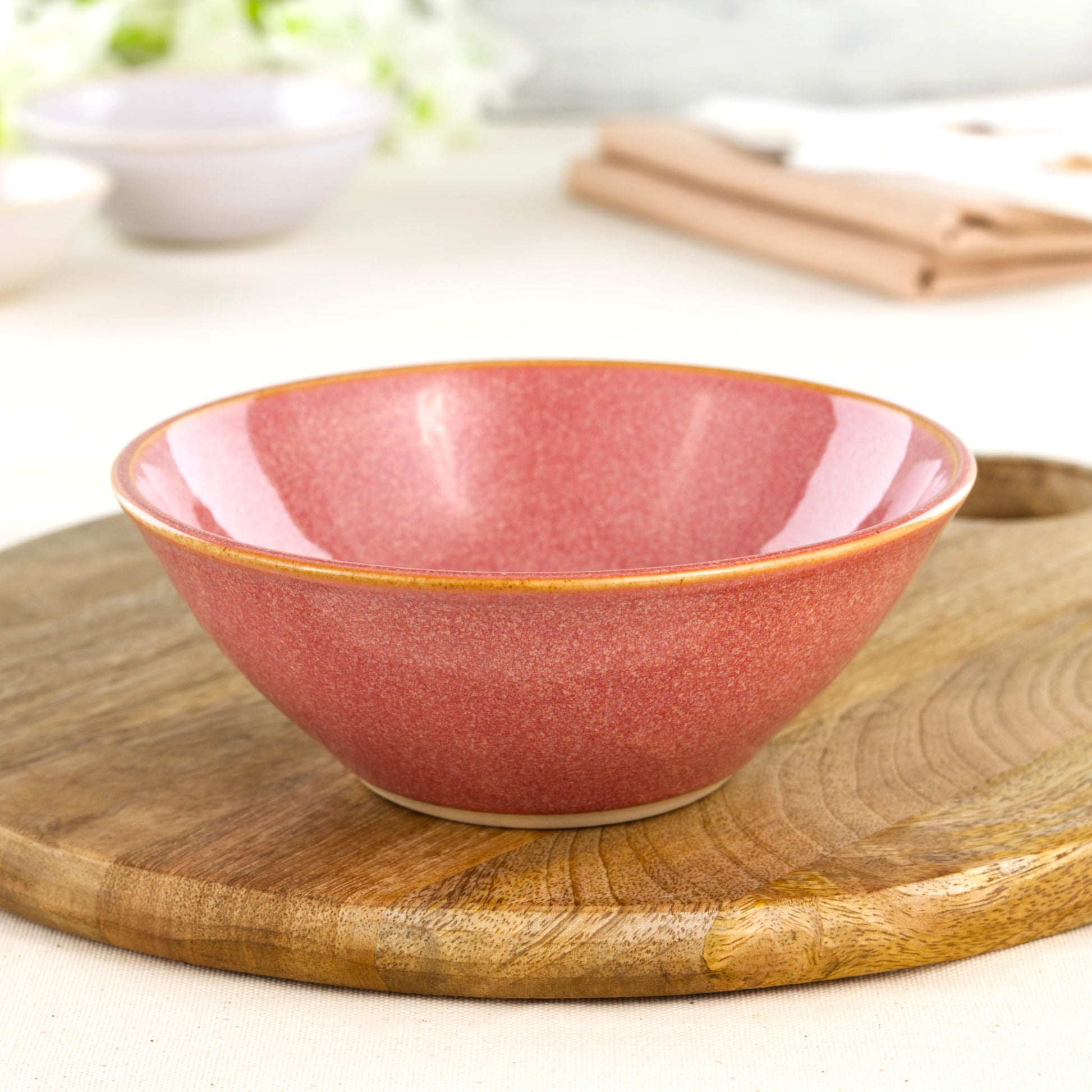 Wheel-thrown Coral medium bowl on a wooden board, handcrafted in a Sussex pottery studio and ideal for pasta, salads or colourful modern table settings