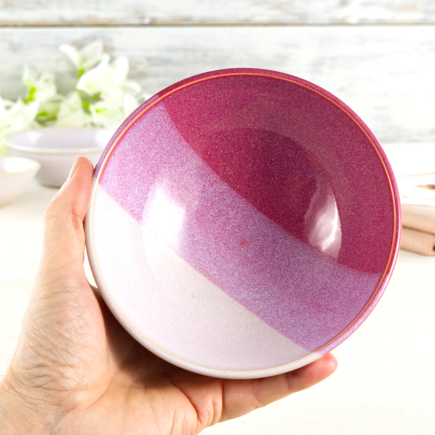 Medium handmade ceramic bowl held in the hand, showing the crimson red and white glazed interior, speckled finish and everyday serving bowl size